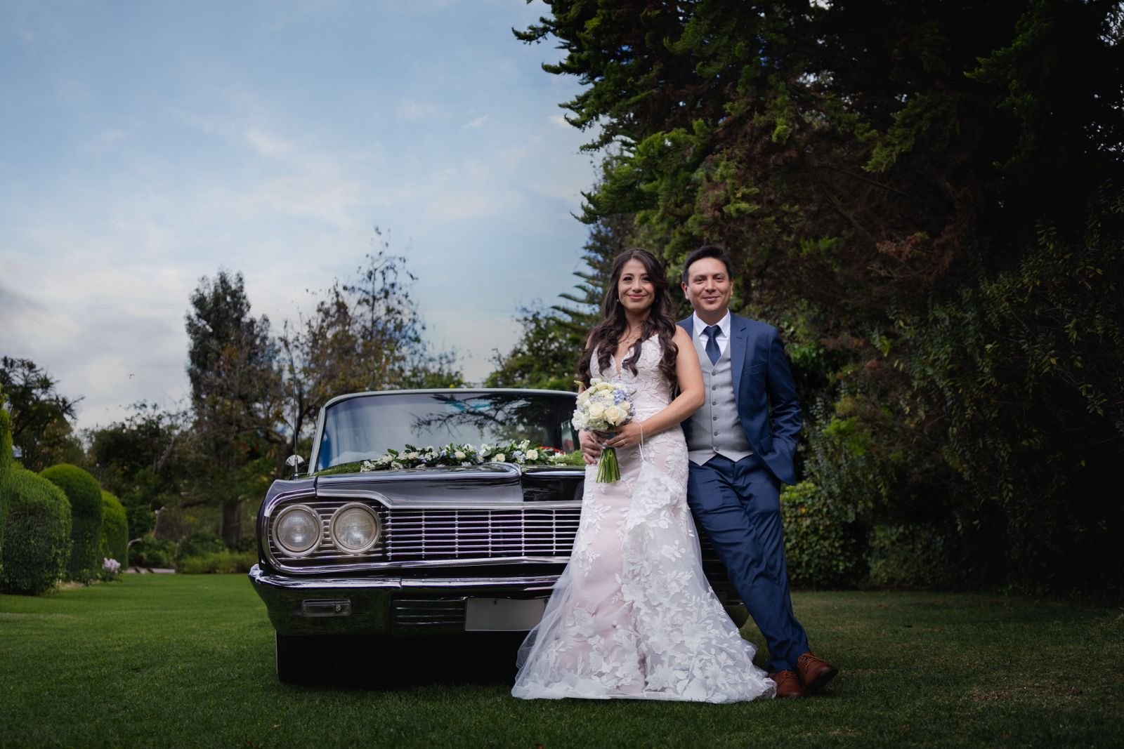 Una pareja de novios junto a un automóvil clásico en un jardín